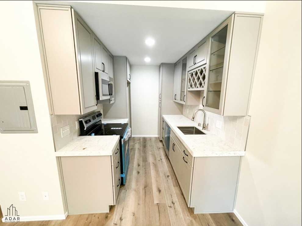 Photo of a small modern galley separate kitchen in Los Angeles with an undermount sink, beaded inset cabinets, grey cabinets, marble benchtops, white splashback, ceramic splashback, stainless steel appliances, light hardwood floors, brown floor and white benchtop.