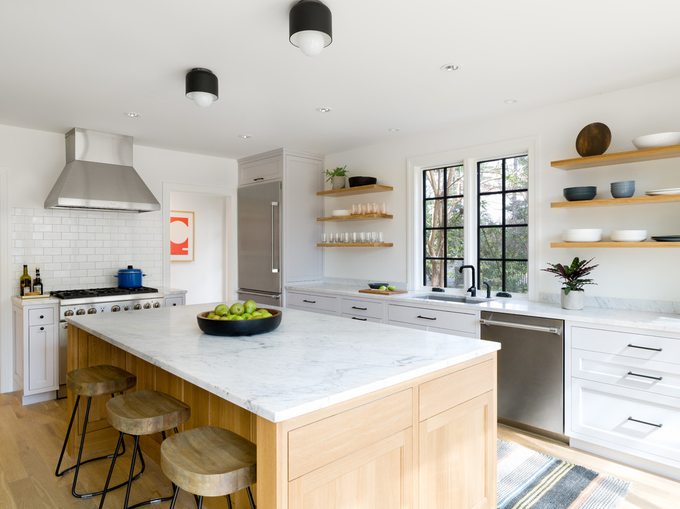 Photo of a large transitional l-shaped separate kitchen in Other with an undermount sink, shaker cabinets, marble benchtops, panelled appliances, light hardwood floors, with island, marble splashback, white benchtop, white cabinets, white splashback and beige floor.