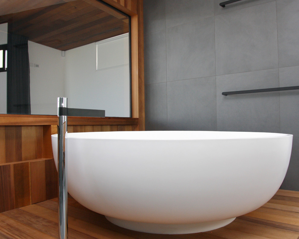Photo of a large contemporary master bathroom in Adelaide with furniture-like cabinets, medium wood cabinets, a freestanding tub, an open shower, a one-piece toilet, gray tile, cement tile, grey walls, cement tiles, a vessel sink, wood benchtops, grey floor and a hinged shower door.