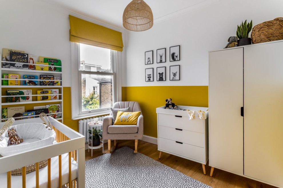 Immagine di una piccola cameretta per neonati neutra classica con pareti gialle e pavimento in legno massello medio