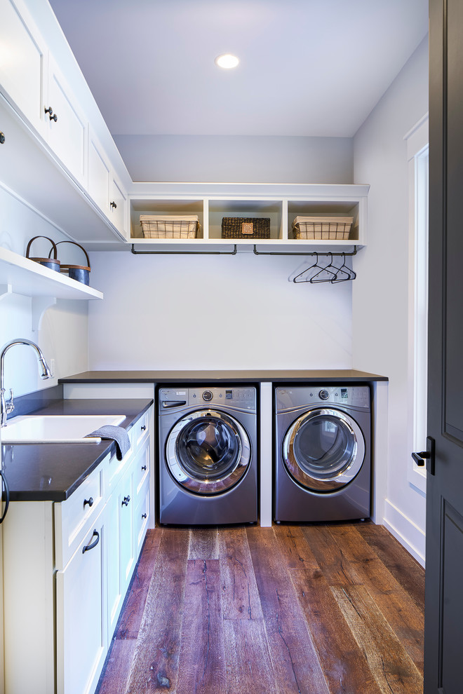 Design ideas for a mid-sized transitional l-shaped dedicated laundry room in Atlanta with a drop-in sink, shaker cabinets, white cabinets, quartz benchtops, grey walls, dark hardwood floors, a side-by-side washer and dryer and black benchtop.