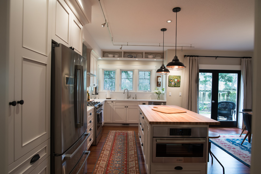 Inspiration for a mid-sized transitional l-shaped medium tone wood floor and brown floor eat-in kitchen remodel in Seattle with an undermount sink, recessed-panel cabinets, white cabinets, quartz countertops, white backsplash, ceramic backsplash, stainless steel appliances, an island and white countertops