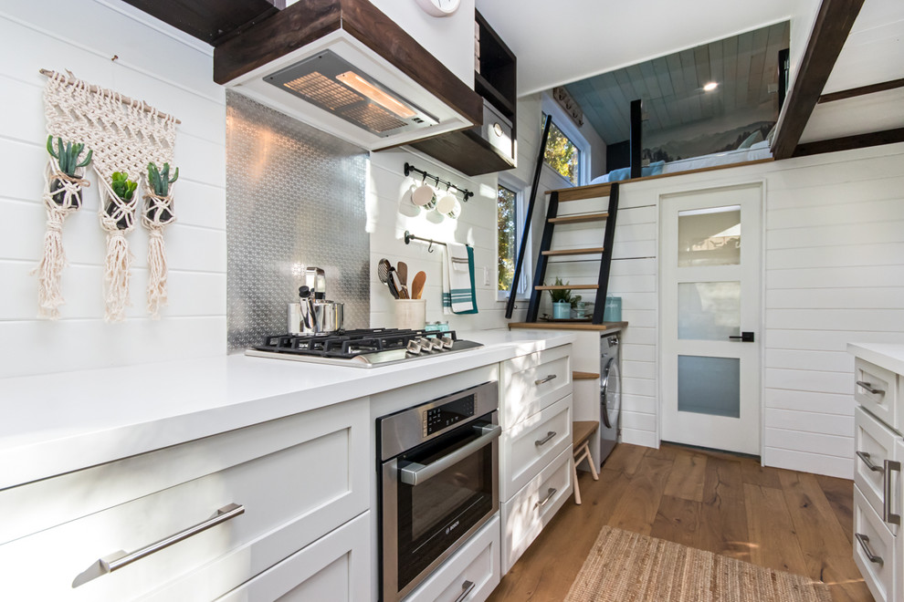 Small beach style galley kitchen in Other with solid surface benchtops, stainless steel appliances, medium hardwood floors, white benchtop, shaker cabinets, grey cabinets, metallic splashback and metal splashback.