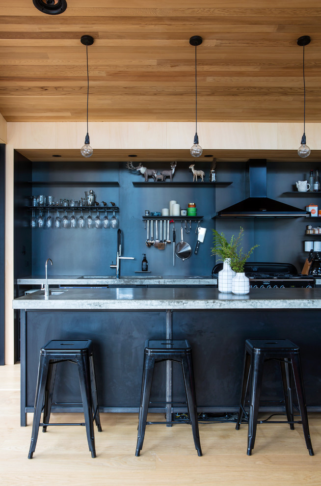 Photo of an industrial kitchen in Auckland with an undermount sink, black splashback, black appliances, light hardwood floors and with island.