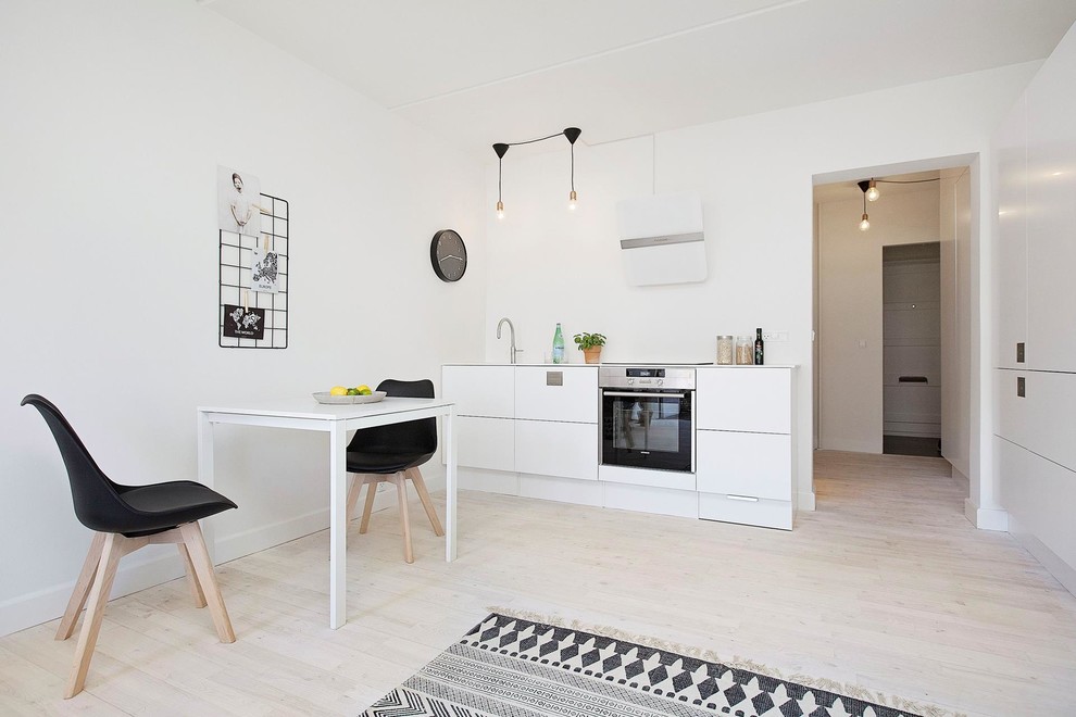 Photo of a mid-sized scandinavian single-wall eat-in kitchen in Copenhagen with a single-bowl sink, flat-panel cabinets, white cabinets, laminate benchtops, stainless steel appliances, light hardwood floors and no island.