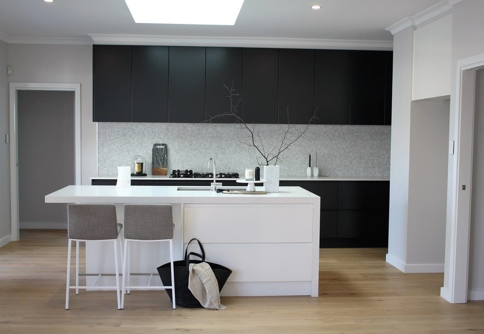 Mid-sized contemporary galley kitchen pantry in Sydney with a double-bowl sink, recessed-panel cabinets, white cabinets, quartzite benchtops, grey splashback, ceramic splashback, black appliances, light hardwood floors and with island.
