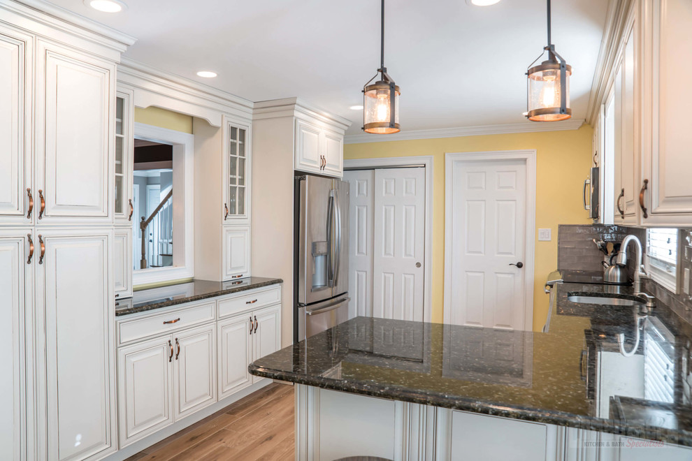 Photo of a mid-sized galley eat-in kitchen in New York with an undermount sink, raised-panel cabinets, yellow cabinets, granite benchtops, grey splashback, cement tile splashback, stainless steel appliances, plywood floors, a peninsula and beige floor.