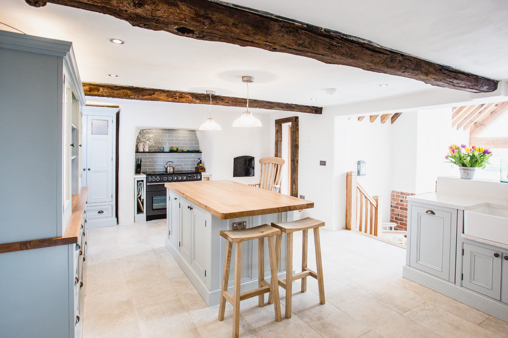 Large country kitchen in West Midlands with a farmhouse sink, blue cabinets, with island, beige floor, recessed-panel cabinets, wood benchtops, grey splashback, black appliances and beige benchtop.