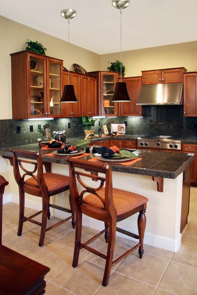 This is an example of a small traditional l-shaped eat-in kitchen in Los Angeles with recessed-panel cabinets, dark wood cabinets, granite benchtops, black splashback, stainless steel appliances, travertine floors and a peninsula.