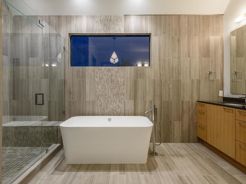 Photo of a large contemporary master bathroom in Austin with flat-panel cabinets, medium wood cabinets, a freestanding tub, a corner shower, gray tile, stone tile, grey walls, travertine floors, an undermount sink and engineered quartz benchtops.