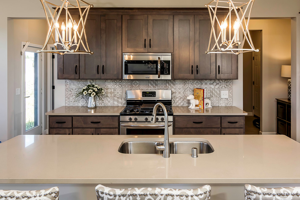 Photo of a mid-sized transitional l-shaped eat-in kitchen in Minneapolis with dark wood cabinets, grey splashback, stainless steel appliances, with island, a double-bowl sink, shaker cabinets, solid surface benchtops and light hardwood floors.