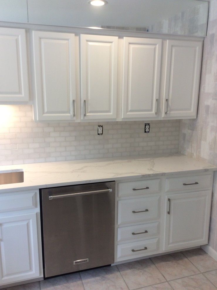 Inspiration for a mid-sized traditional single-wall separate kitchen in New York with an undermount sink, raised-panel cabinets, white cabinets, soapstone benchtops, white splashback, stone tile splashback, stainless steel appliances, ceramic floors and beige floor.