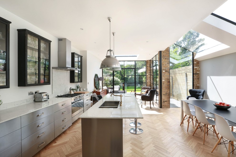 Large contemporary eat-in kitchen in London with a double-bowl sink, marble benchtops, white splashback, marble splashback, stainless steel appliances, light hardwood floors, beige floor, glass-front cabinets, black cabinets and with island.