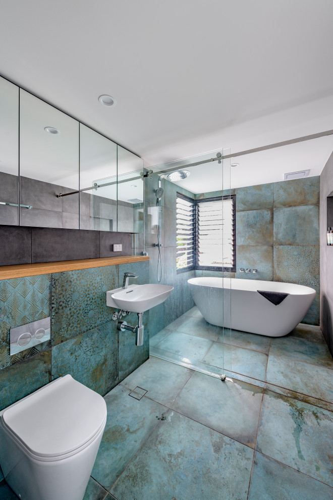 Modelo de cuarto de baño único industrial con baldosas y/o azulejos azules, paredes grises, ducha con puerta corredera, bañera exenta y suelo azul