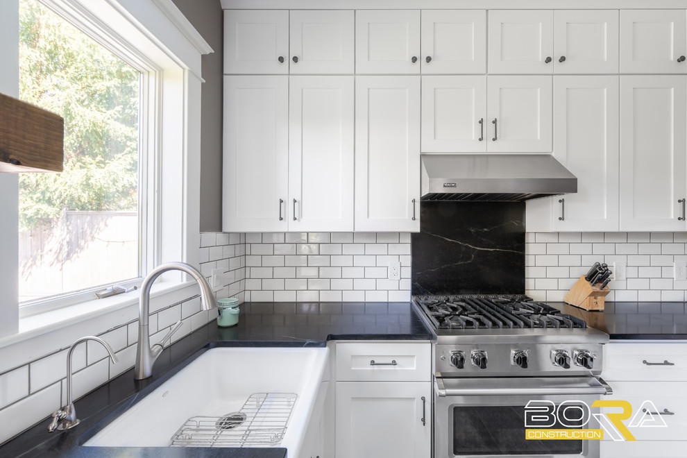 Example of a mid-sized transitional u-shaped ceramic tile and gray floor eat-in kitchen design in Seattle with a farmhouse sink, shaker cabinets, white cabinets, quartz countertops, white backsplash, ceramic backsplash, stainless steel appliances, a peninsula and black countertops