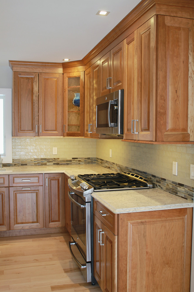 Open concept kitchen - large transitional u-shaped light wood floor and beige floor open concept kitchen idea in Boston with an undermount sink, raised-panel cabinets, medium tone wood cabinets, quartz countertops, multicolored backsplash, glass tile backsplash, stainless steel appliances, an island and beige countertops