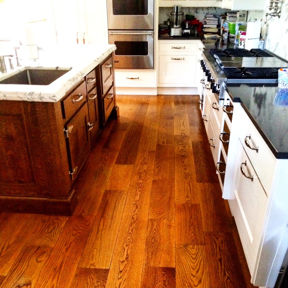Example of a large mountain style u-shaped medium tone wood floor enclosed kitchen design in New York with white cabinets, white backsplash, stone slab backsplash, an island, an undermount sink, shaker cabinets, solid surface countertops and stainless steel appliances