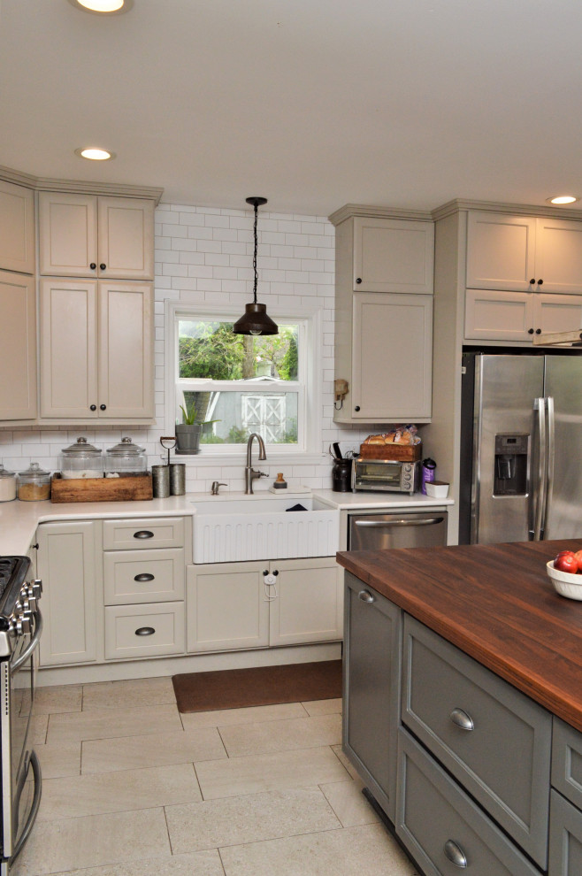 This is an example of a large country l-shaped open plan kitchen in Other with a farmhouse sink, recessed-panel cabinets, beige cabinets, quartzite benchtops, white splashback, subway tile splashback, stainless steel appliances, ceramic floors, with island, beige floor and white benchtop.