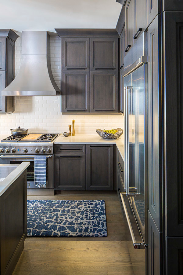 Photo of a mid-sized transitional l-shaped open plan kitchen in Chicago with a farmhouse sink, shaker cabinets, grey cabinets, quartz benchtops, white splashback, subway tile splashback, stainless steel appliances, medium hardwood floors and with island.