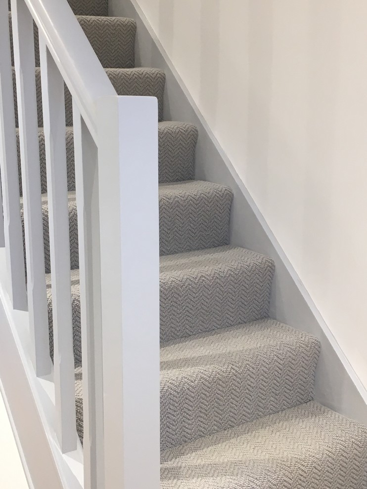 Photo of a contemporary carpeted straight staircase in Hertfordshire with carpet risers and wood railing.