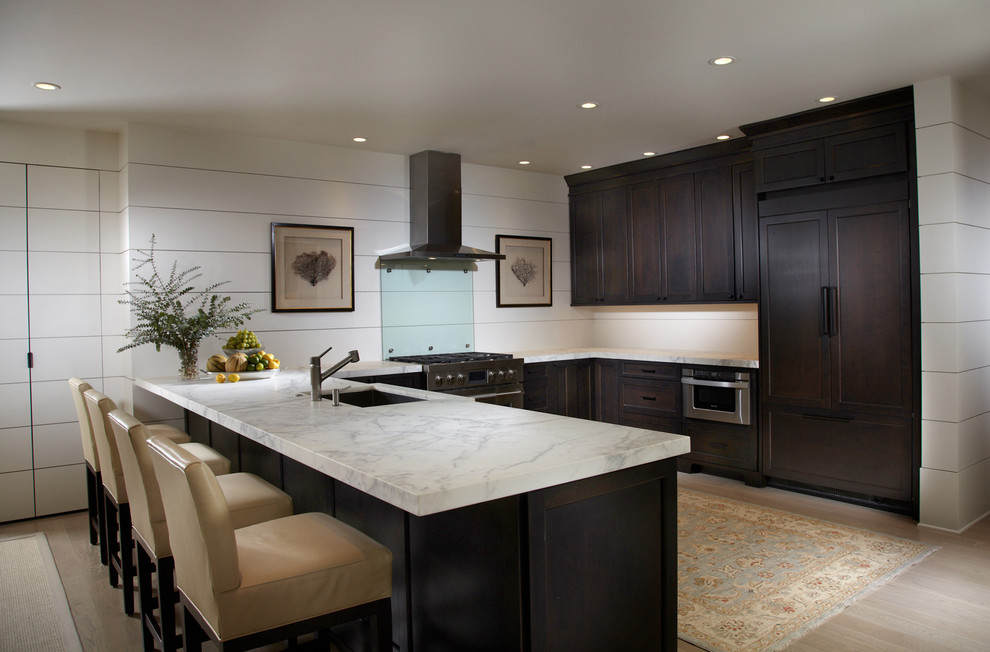 Inspiration for a mid-sized traditional u-shaped eat-in kitchen in Miami with an undermount sink, flat-panel cabinets, dark wood cabinets, marble benchtops, white splashback, stainless steel appliances and light hardwood floors.