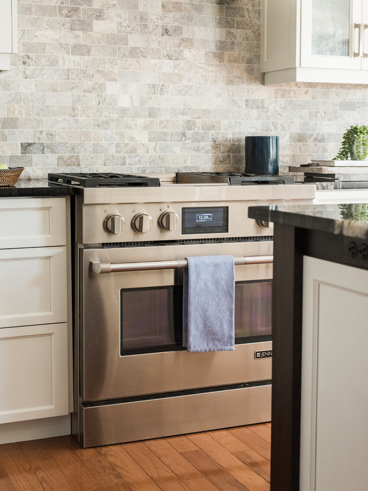 Inspiration for a transitional medium tone wood floor and brown floor kitchen remodel in Toronto with an undermount sink, recessed-panel cabinets, white cabinets, granite countertops, gray backsplash, travertine backsplash, stainless steel appliances and an island