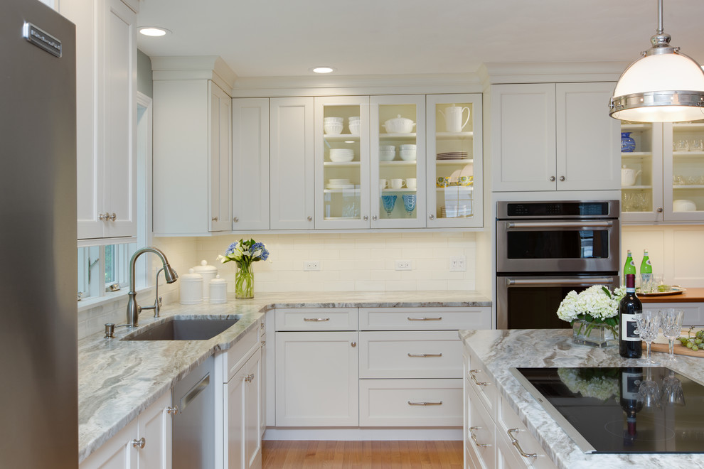 Example of a transitional l-shaped light wood floor eat-in kitchen design in Boston with an undermount sink, recessed-panel cabinets, white cabinets, quartzite countertops, white backsplash, subway tile backsplash, stainless steel appliances and an island