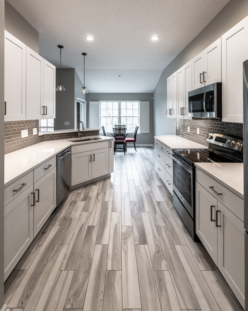 Mid-sized transitional galley porcelain tile and multicolored floor eat-in kitchen photo with an undermount sink, recessed-panel cabinets, white cabinets, quartz countertops, gray backsplash, ceramic backsplash, stainless steel appliances, a peninsula and white countertops