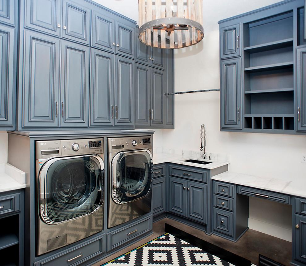 Design ideas for a large transitional l-shaped dedicated laundry room in Oklahoma City with a farmhouse sink, raised-panel cabinets, blue cabinets, marble benchtops, white walls, concrete floors, a side-by-side washer and dryer and white benchtop.