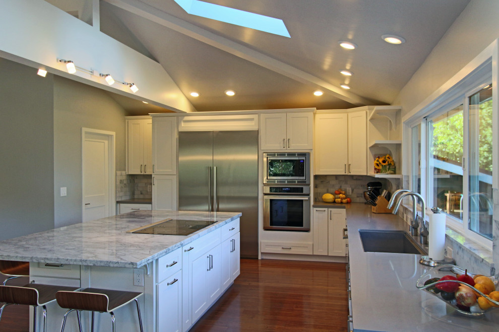 Kitchen - large u-shaped medium tone wood floor and brown floor kitchen idea with an undermount sink, shaker cabinets, white cabinets, quartzite countertops, multicolored backsplash, stone tile backsplash, stainless steel appliances, an island and multicolored countertops