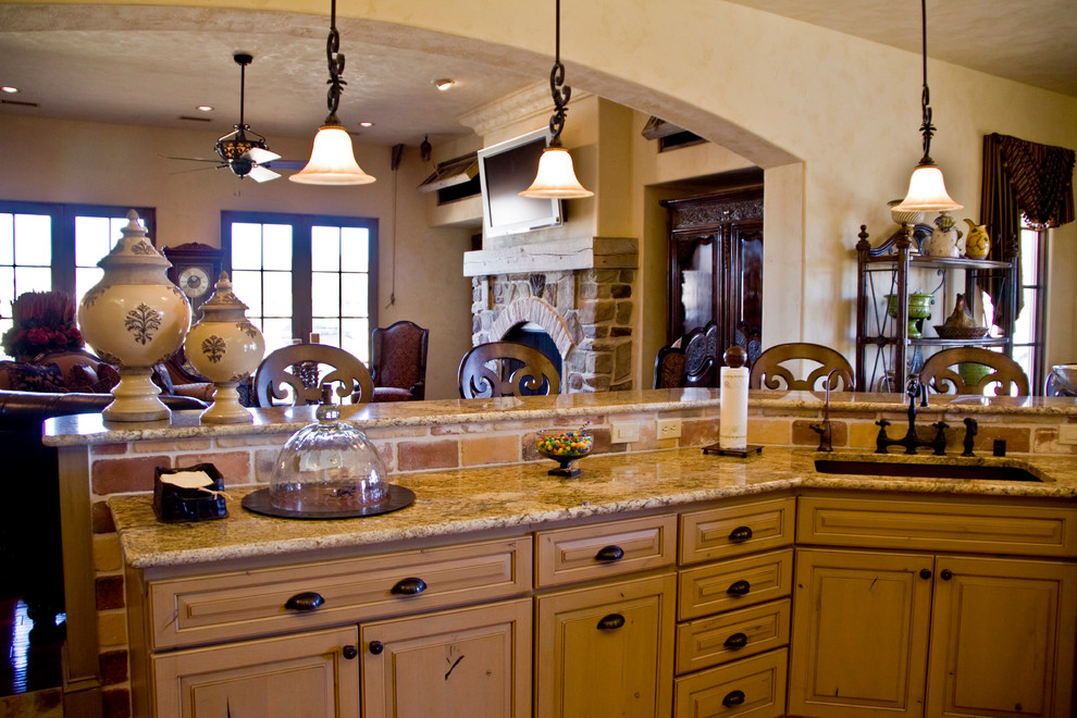 This is an example of a mediterranean eat-in kitchen in Austin with raised-panel cabinets, light wood cabinets, granite benchtops, beige splashback, stone tile splashback and with island.