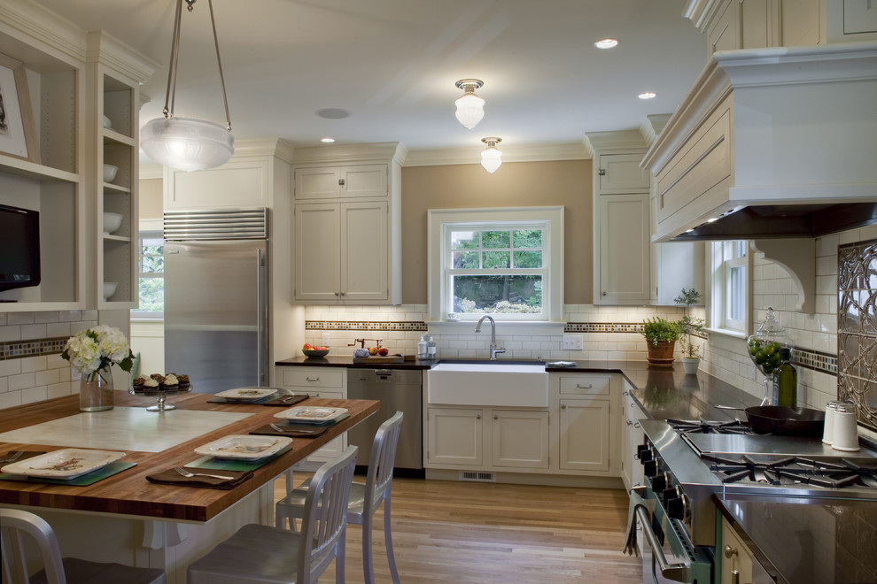 This is an example of a large traditional u-shaped eat-in kitchen in Portland with a farmhouse sink, shaker cabinets, white cabinets, white splashback, subway tile splashback, stainless steel appliances, light hardwood floors and no island.