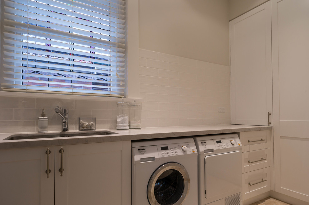 Transitional utility room in Other with a double-bowl sink, shaker cabinets, white splashback, white walls, a side-by-side washer and dryer and beige floor.
