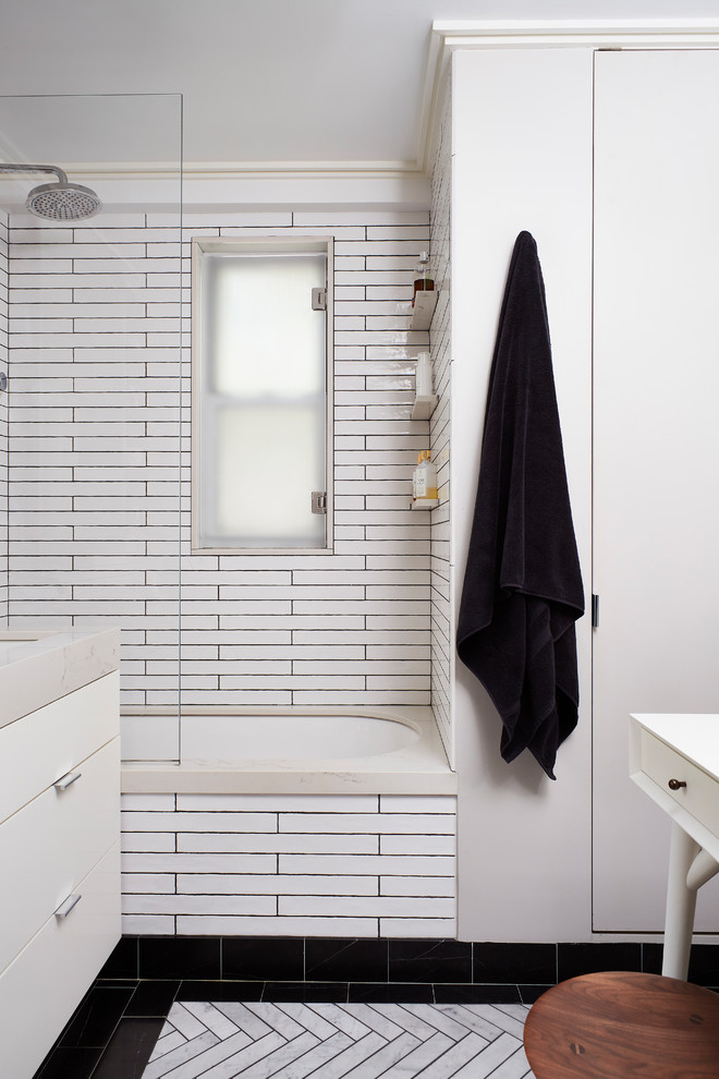 This is an example of a small modern kids bathroom in New York with flat-panel cabinets, white cabinets, a drop-in tub, a shower/bathtub combo, a one-piece toilet, black and white tile, ceramic tile, grey walls, marble floors, an undermount sink, engineered quartz benchtops, grey floor, an open shower and multi-coloured benchtops.