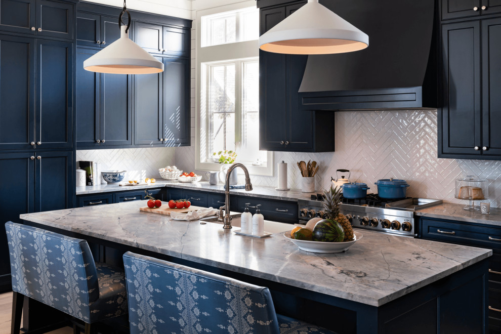 Photo of a beach style l-shaped kitchen in Dallas with a farmhouse sink, recessed-panel cabinets, blue cabinets, white splashback, stainless steel appliances, with island and grey benchtop.