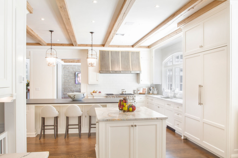 Large traditional l-shaped kitchen/diner in New York with shaker cabinets, white cabinets, engineered stone countertops, white splashback, engineered quartz splashback, painted wood flooring, multiple islands, brown floors, black worktops and exposed beams.