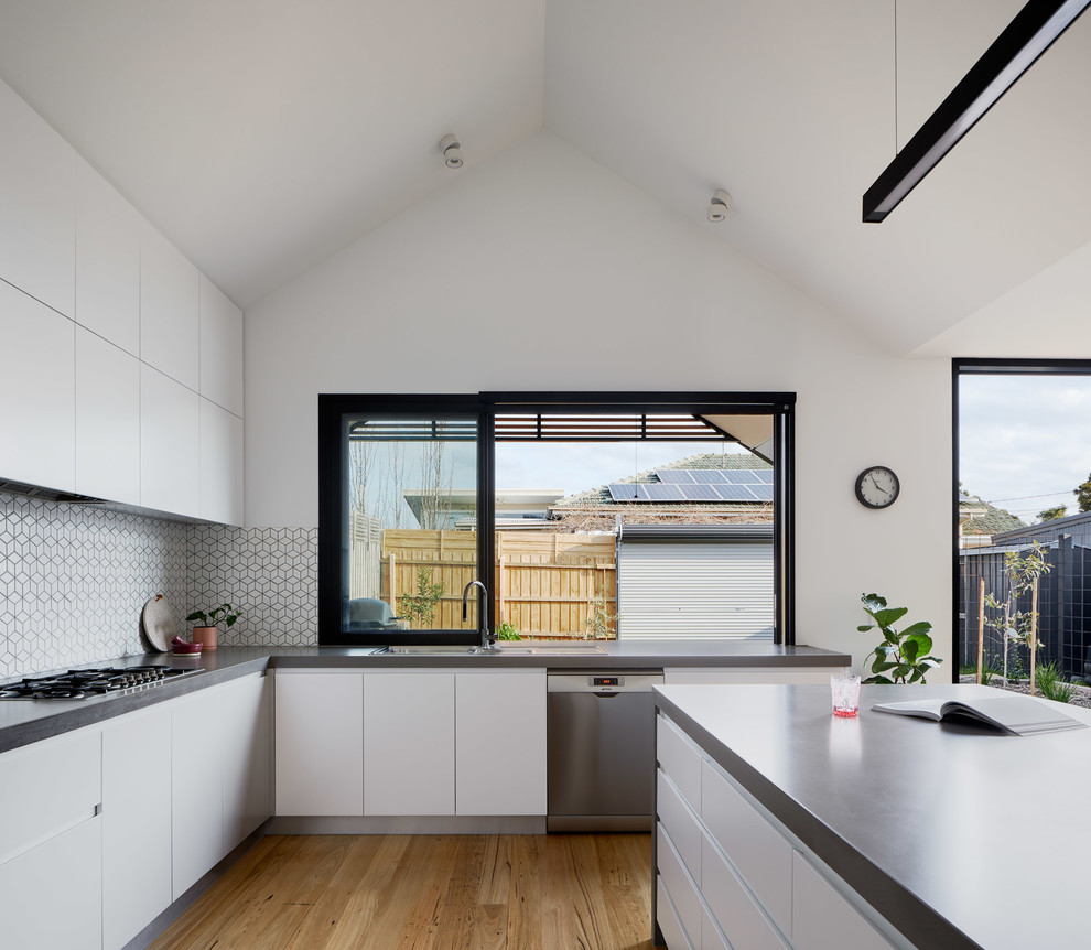 Large contemporary u-shaped open plan kitchen in Melbourne with flat-panel cabinets, white cabinets, quartz benchtops, ceramic splashback, stainless steel appliances, with island, grey benchtop, a drop-in sink, multi-coloured splashback, medium hardwood floors and beige floor.