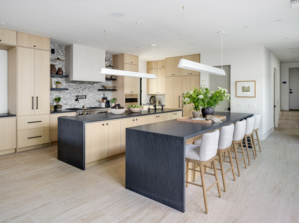 This is an example of a large contemporary eat-in kitchen in Orange County with a farmhouse sink, flat-panel cabinets, wood benchtops, multi-coloured splashback, porcelain splashback, panelled appliances, porcelain floors, multiple islands, beige floor and black benchtop.