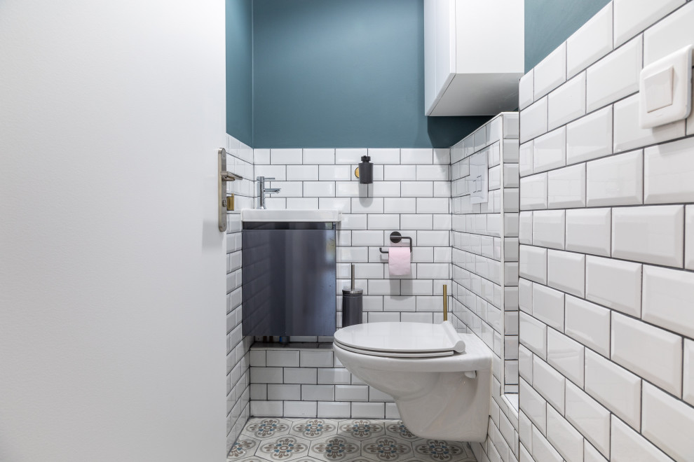 This is an example of a mid-sized contemporary powder room in Paris with a wall-mount toilet, white tile, subway tile, blue walls, cement tiles, a wall-mount sink and grey floor.