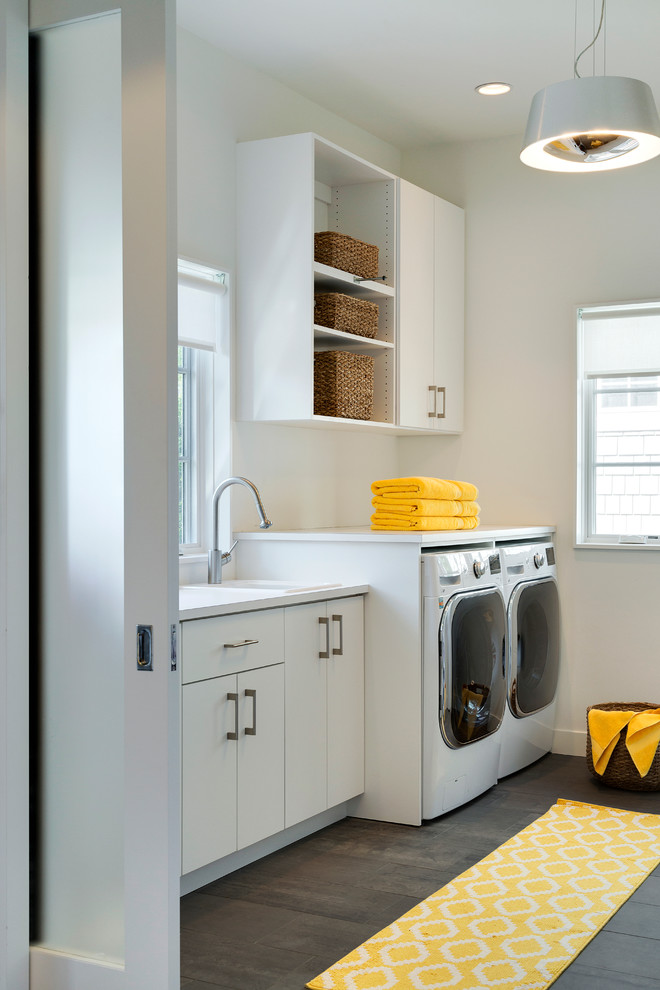 Midcentury galley utility room in Minneapolis with a drop-in sink, flat-panel cabinets, white cabinets, solid surface benchtops, white walls, porcelain floors and a side-by-side washer and dryer.
