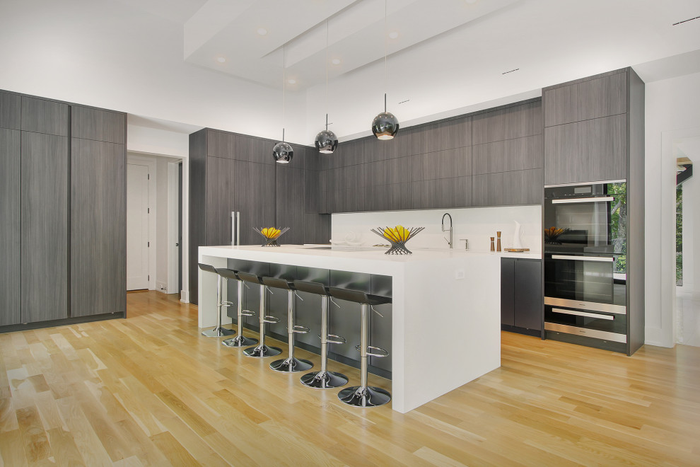 Large trendy u-shaped light wood floor and coffered ceiling open concept kitchen photo in New York with flat-panel cabinets, medium tone wood cabinets, an island, an integrated sink, quartz countertops, white backsplash, quartz backsplash, paneled appliances and white countertops