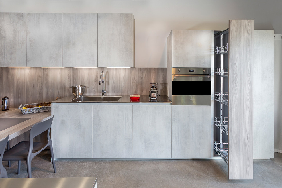 Inspiration for a mid-sized contemporary single-wall eat-in kitchen in Bordeaux with an integrated sink, flat-panel cabinets, grey cabinets, grey splashback, stainless steel appliances, a peninsula, stainless steel benchtops and timber splashback.