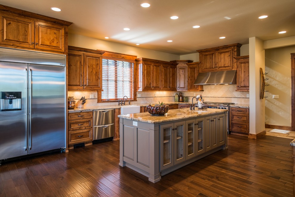 Example of a mountain style dark wood floor eat-in kitchen design with a farmhouse sink, raised-panel cabinets, medium tone wood cabinets, granite countertops, stainless steel appliances and an island