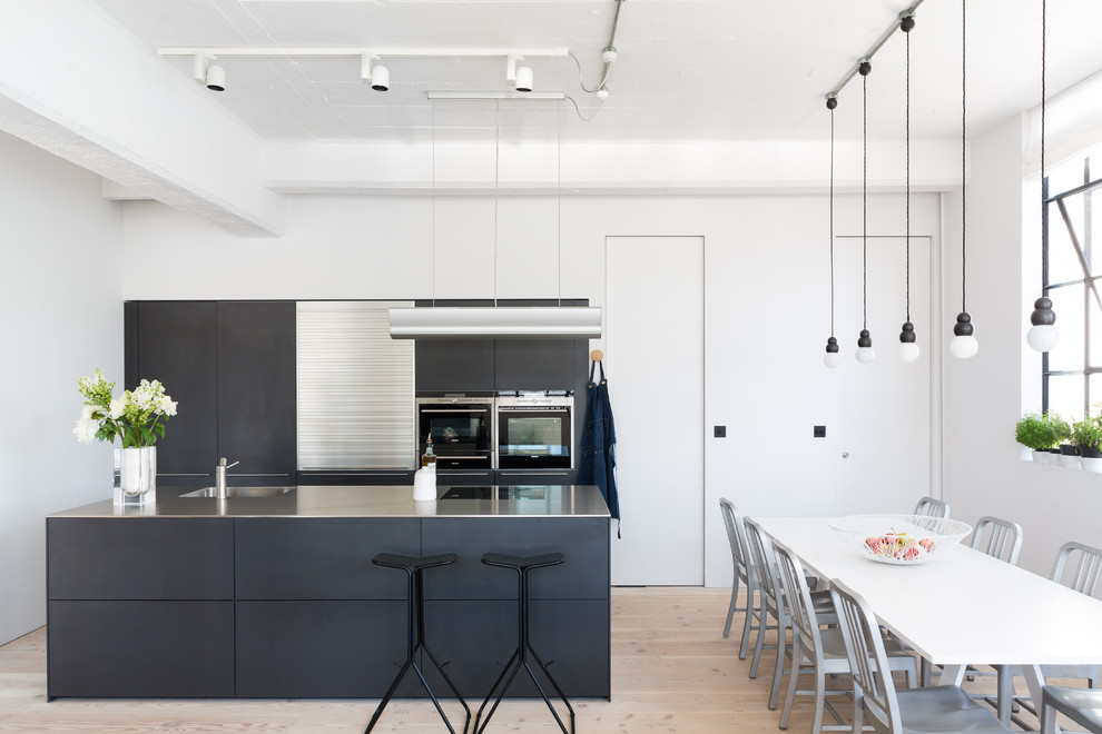 Inspiration for a scandinavian eat-in kitchen in London with an integrated sink, flat-panel cabinets, stainless steel benchtops, stainless steel appliances, light hardwood floors and with island.