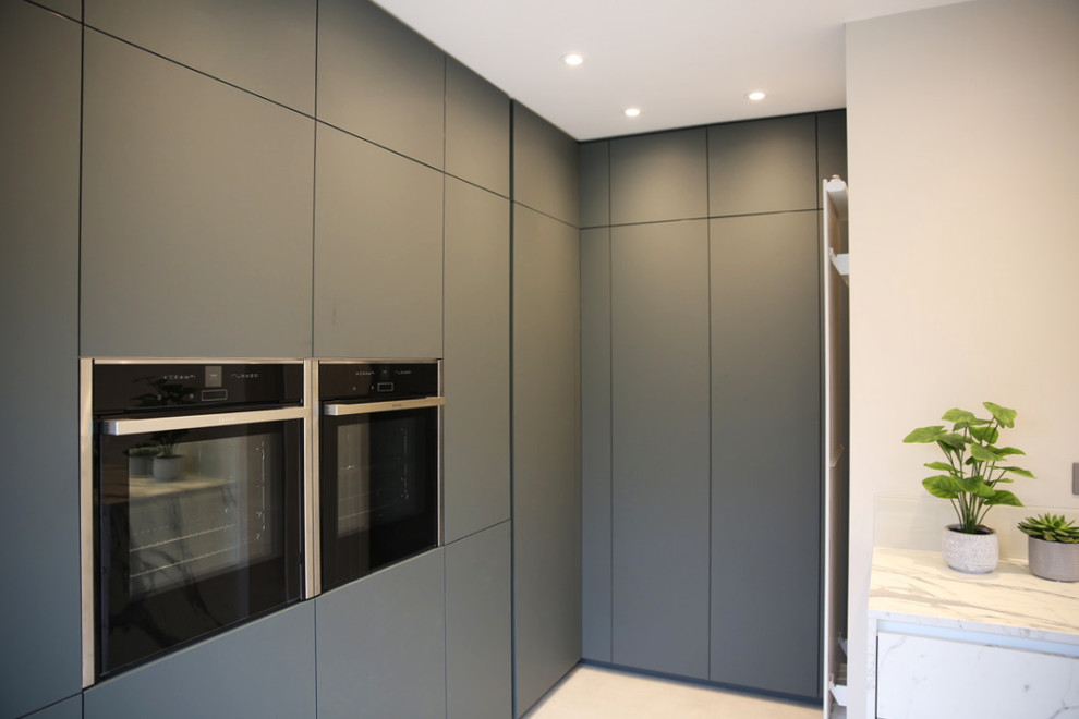Inspiration for a medium sized modern grey and white l-shaped kitchen/diner in London with an integrated sink, flat-panel cabinets, green cabinets, laminate countertops, white splashback, glass sheet splashback, black appliances, laminate floors, no island, beige floors, white worktops and feature lighting.