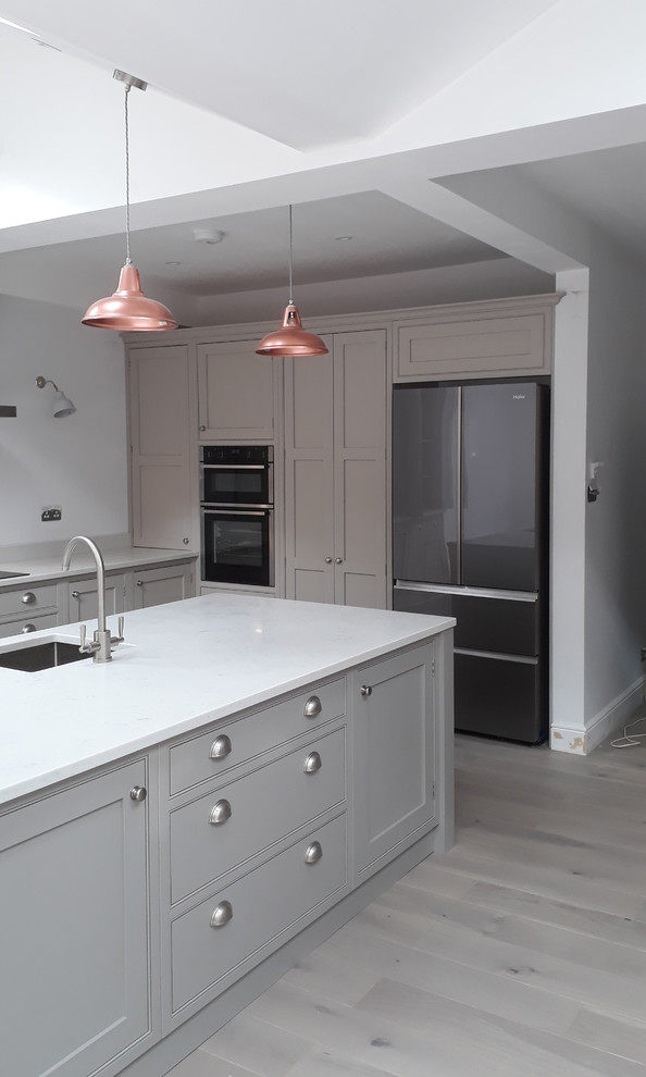 This is an example of a mid-sized traditional l-shaped eat-in kitchen in London with a triple-bowl sink, beaded inset cabinets, grey cabinets, quartzite benchtops, with island and white benchtop.