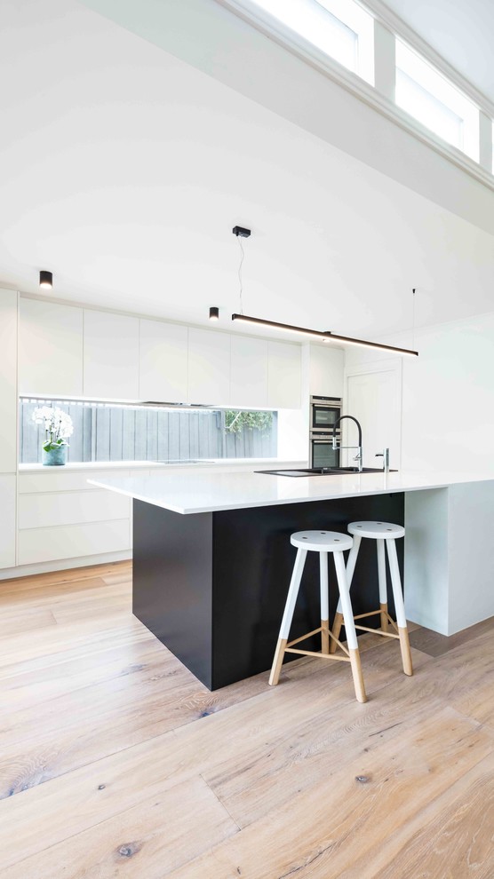 This is an example of a mid-sized contemporary galley kitchen pantry in Melbourne with a double-bowl sink, white cabinets, marble benchtops, window splashback, stainless steel appliances, light hardwood floors and with island.