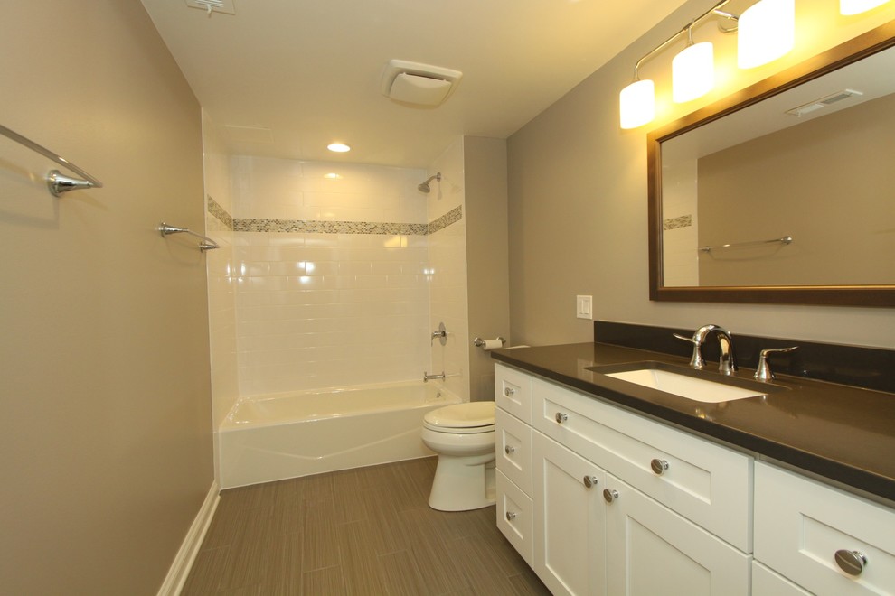 Inspiration for a mid-sized transitional kids bathroom in Chicago with recessed-panel cabinets, white cabinets, an alcove tub, a shower/bathtub combo, a two-piece toilet, white tile, subway tile, beige walls, porcelain floors, an undermount sink, engineered quartz benchtops, grey floor, a shower curtain and black benchtops.