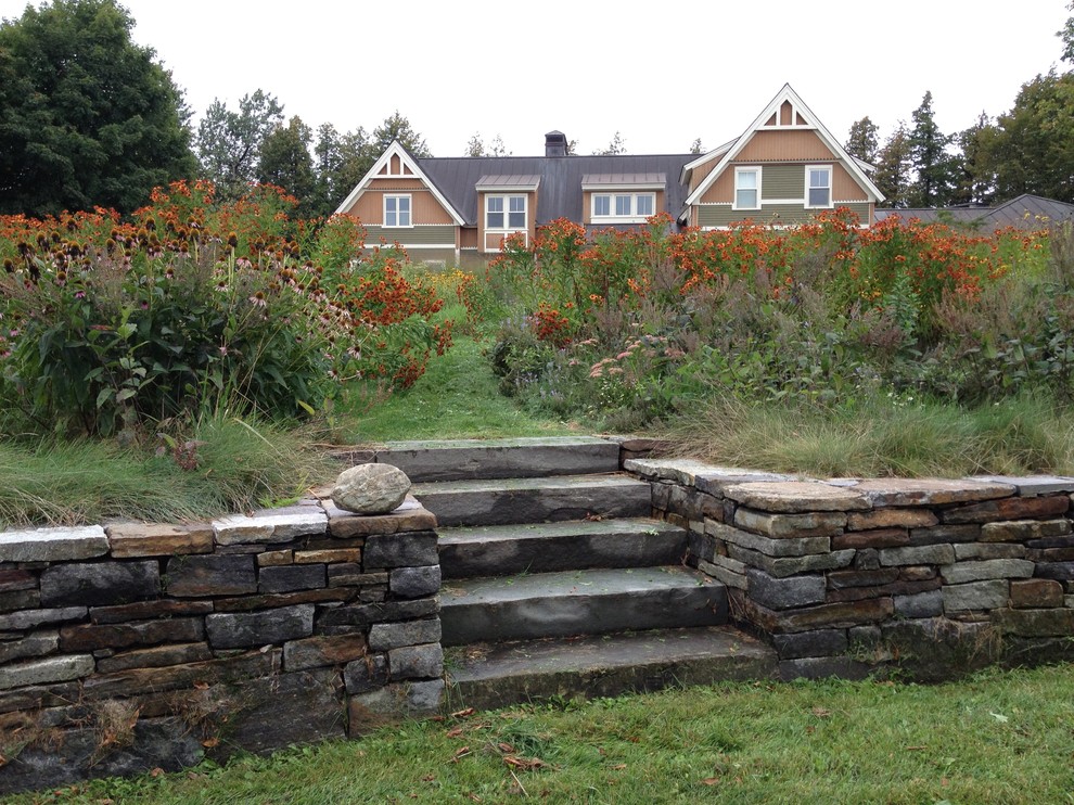 This is an example of a large contemporary sloped full sun garden for summer in Burlington with a garden path and natural stone pavers.
