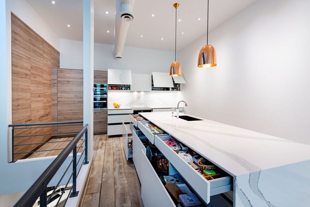 Eat-in kitchen - mid-sized transitional galley medium tone wood floor eat-in kitchen idea in Toronto with an undermount sink, flat-panel cabinets, medium tone wood cabinets, quartz countertops, white backsplash, stainless steel appliances and an island